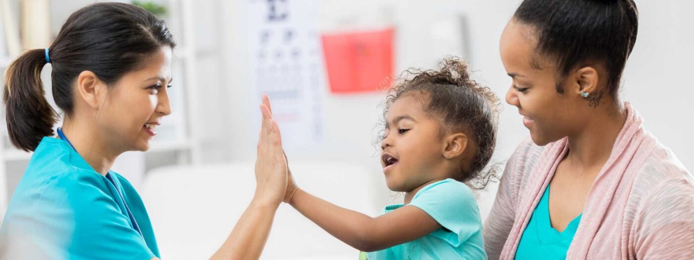 A young child high-fives a clinician while her mother looks on