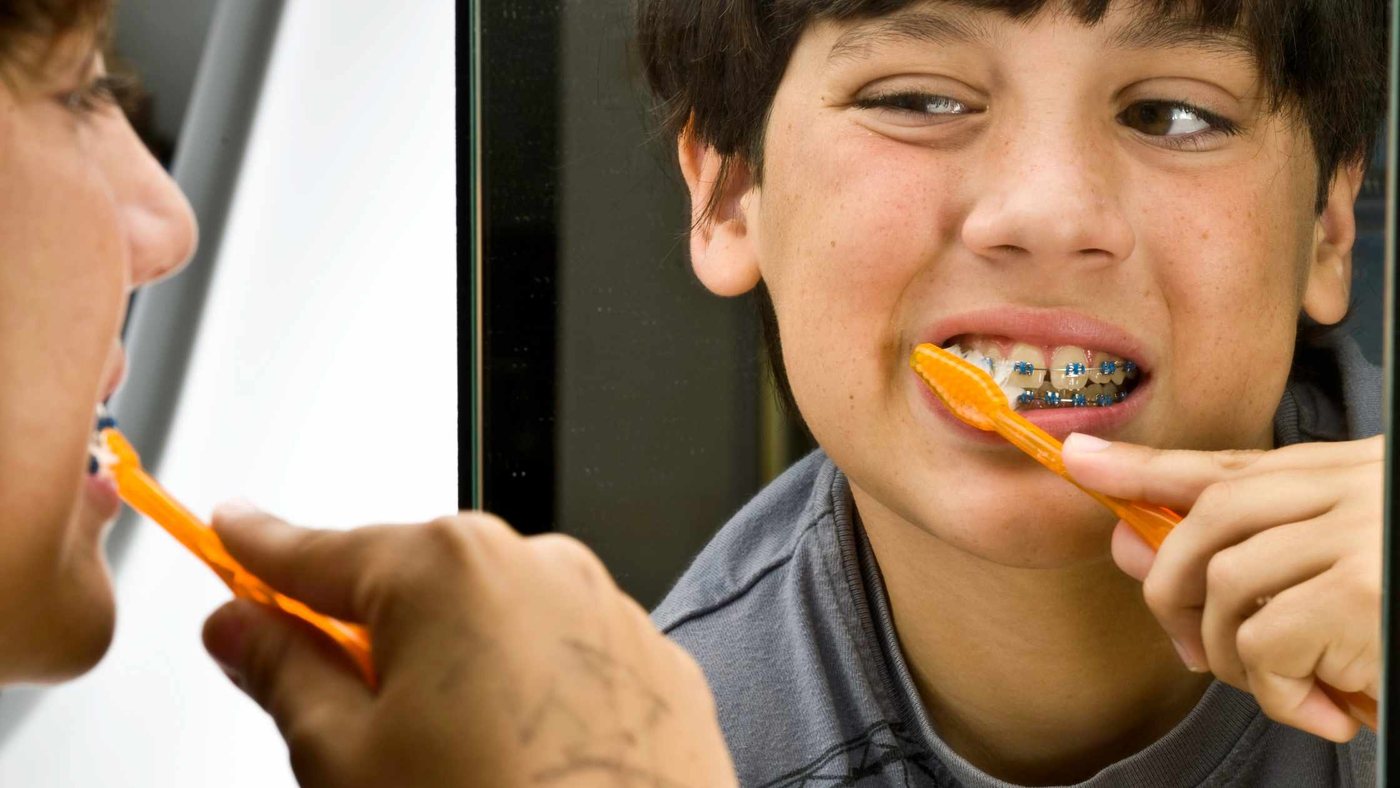 A boy with braces brushing his teeth in front of a mirror