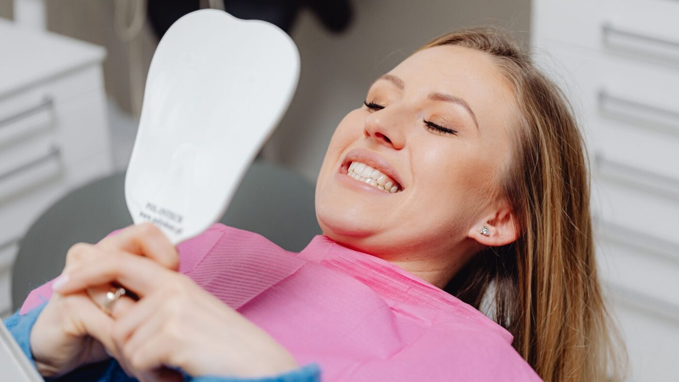 A patient in the dental chair smiling at her whiter teeth in a hand mirror